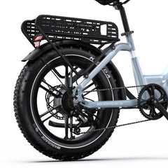 Close-up rear view of a light blue onesport OT08 electric bicycle with a black rear cargo basket, black fender, fat tire, disc brakes, and chainring, on a white studio background.